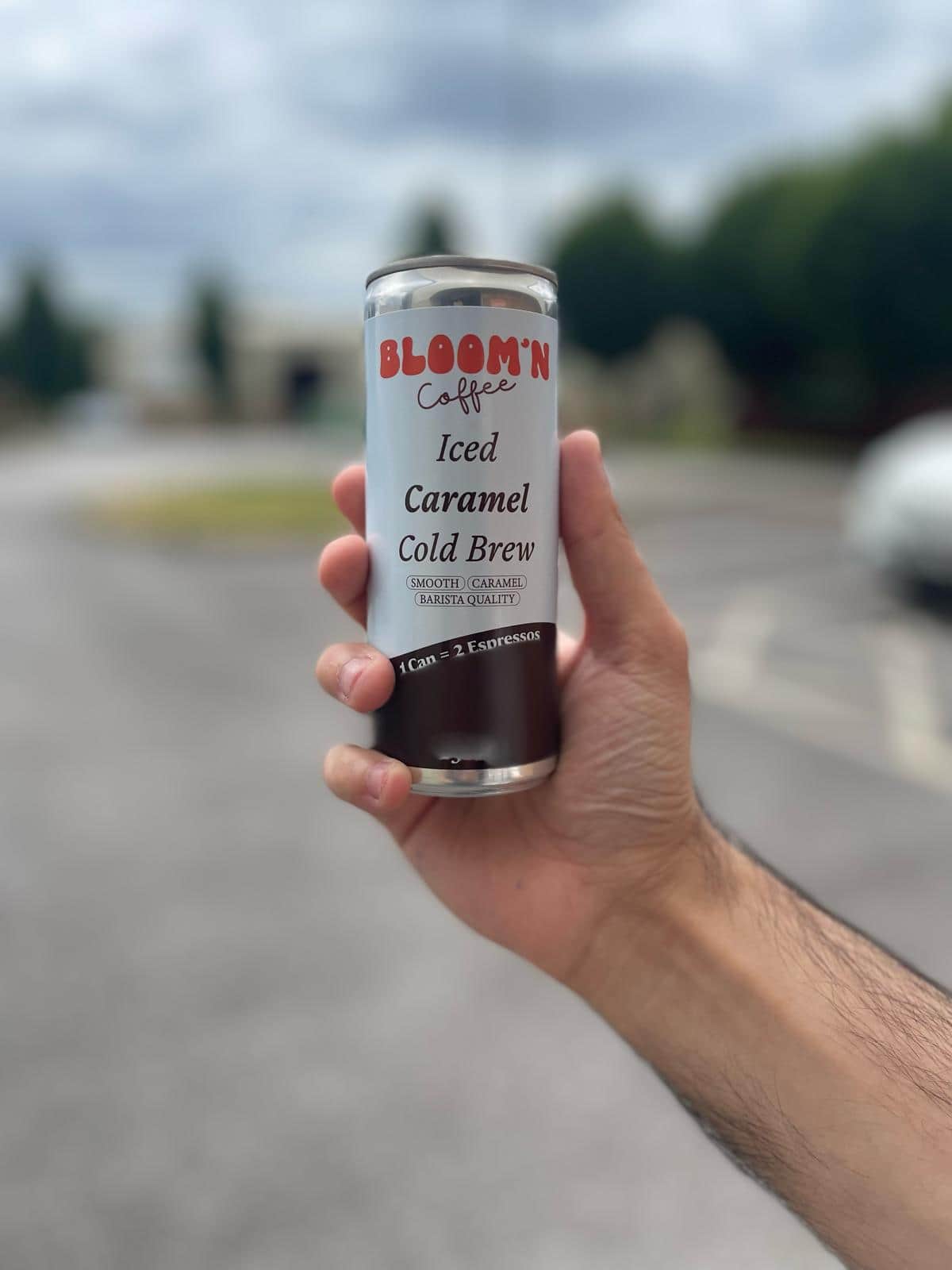 A hand holding up a can of Bloom'n Iced Caramel Cold Brew outdoors