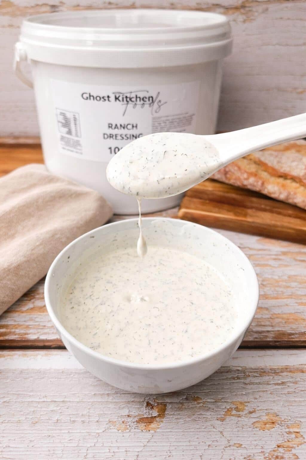 Ghost Kitchen Foods Ranch Dressing in a ten litre tub with a bowl of the dressing and a spoon